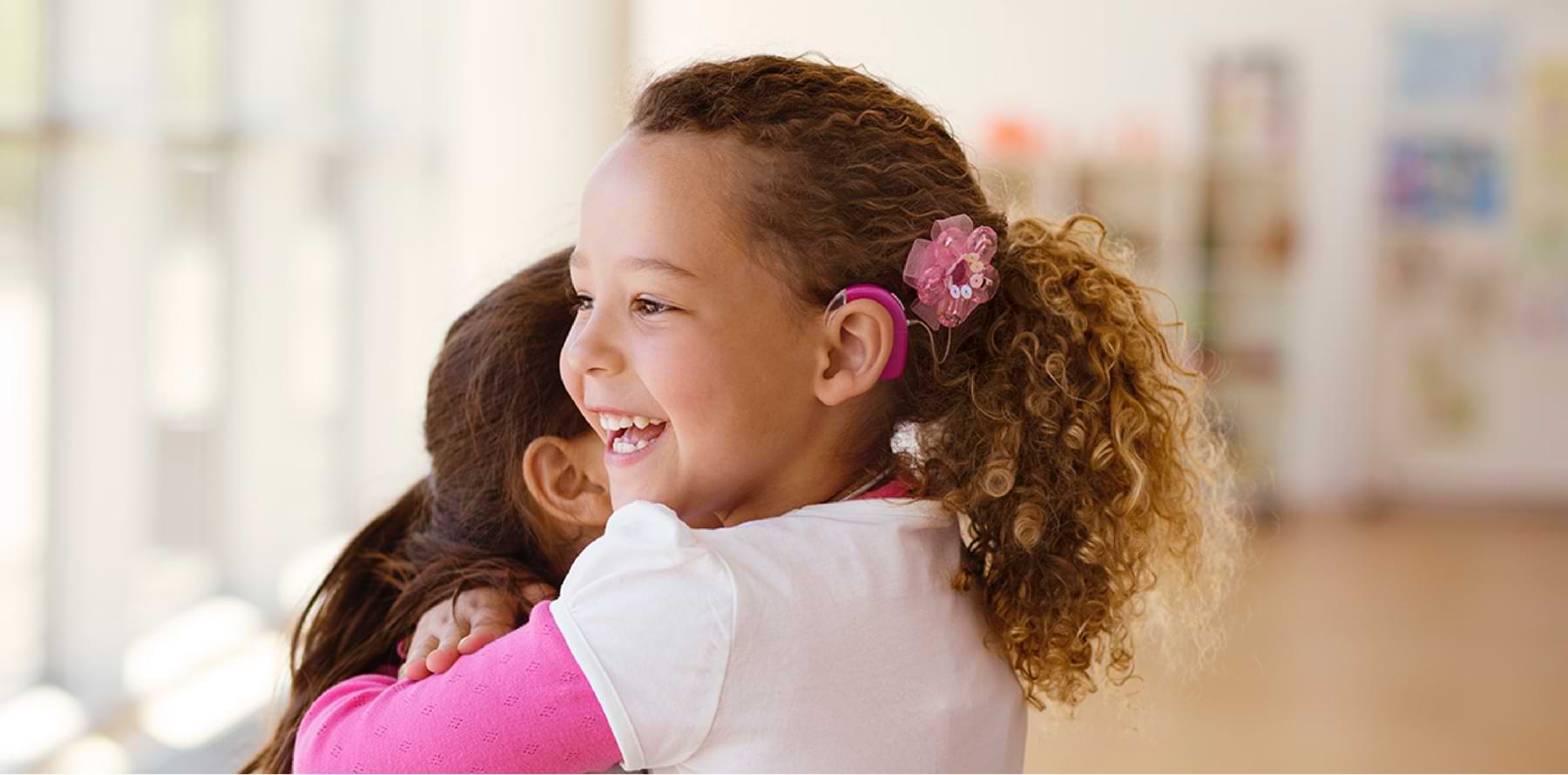 Ein glückliches Kind mit Cochlea Implantat umarmt ein weiteres Kind