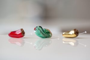 Drei Hörgeräte in rot grün und gold liegen nebeneinander.